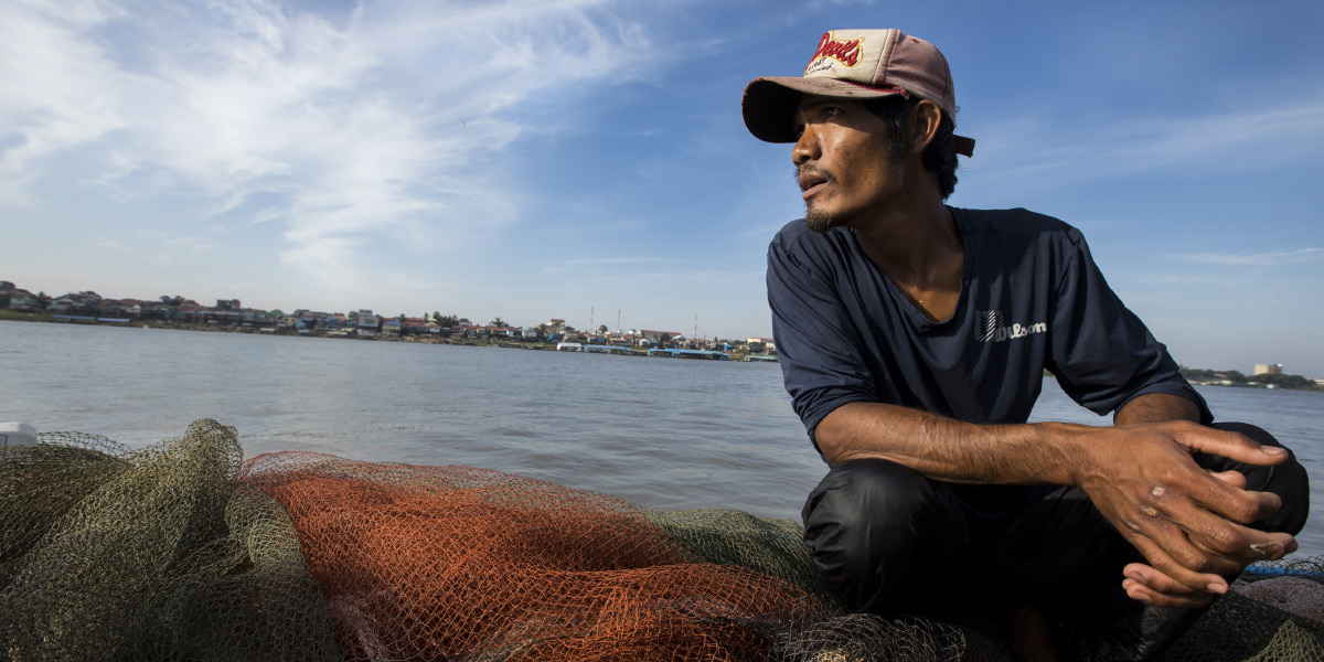 Fisherman sitting on net by Mekong River
