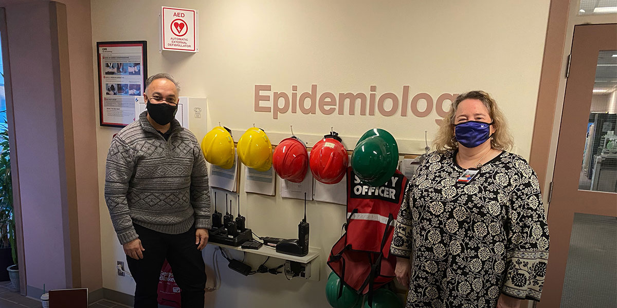 Hilary Godwin and Umair Shah pose socially-distanced with masks in front of a lab