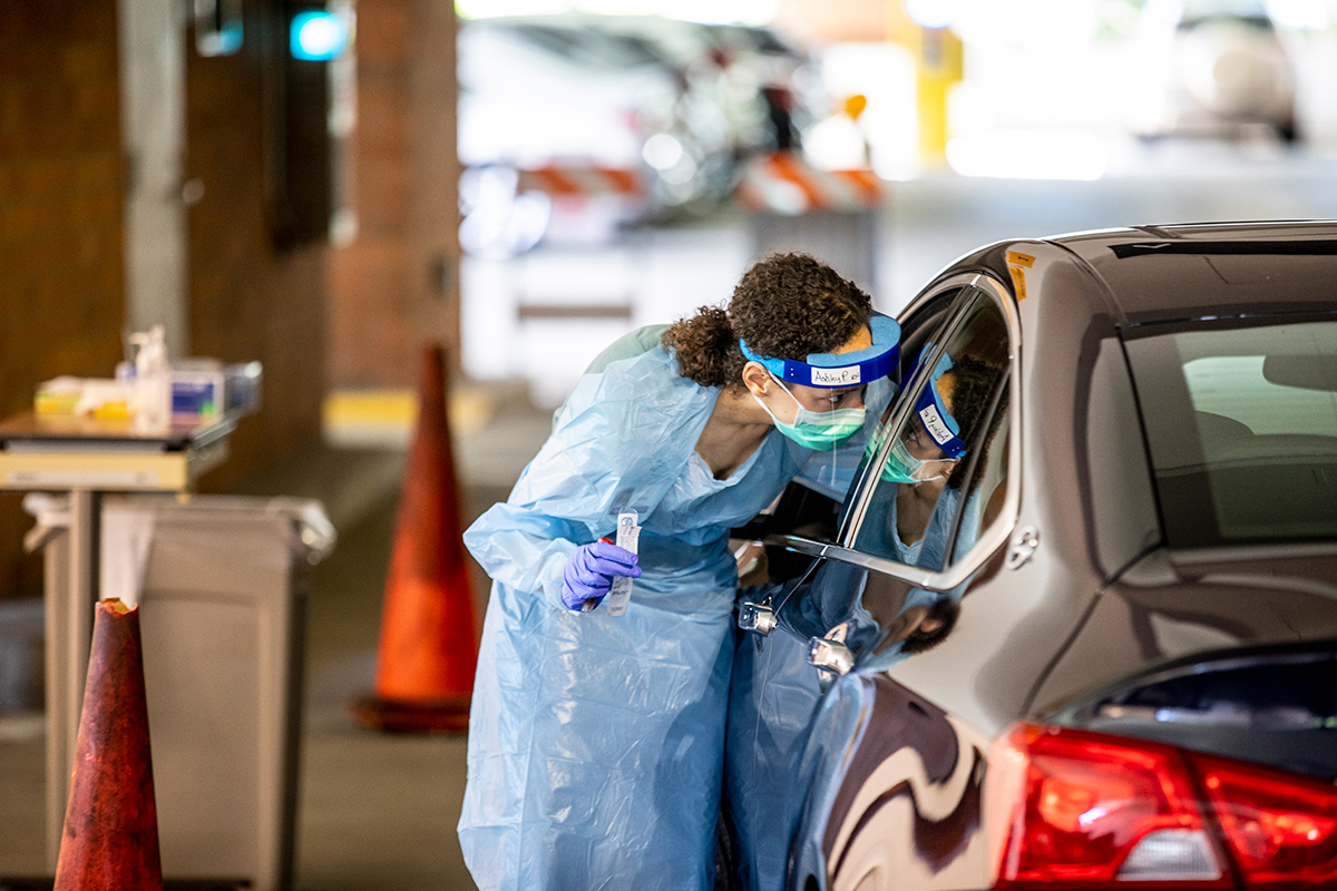 A UW Medicine nurse administers a COVID-19 test through the window of a car