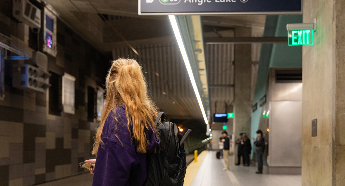 Person stands on light rail platform looking at group of people in the distance