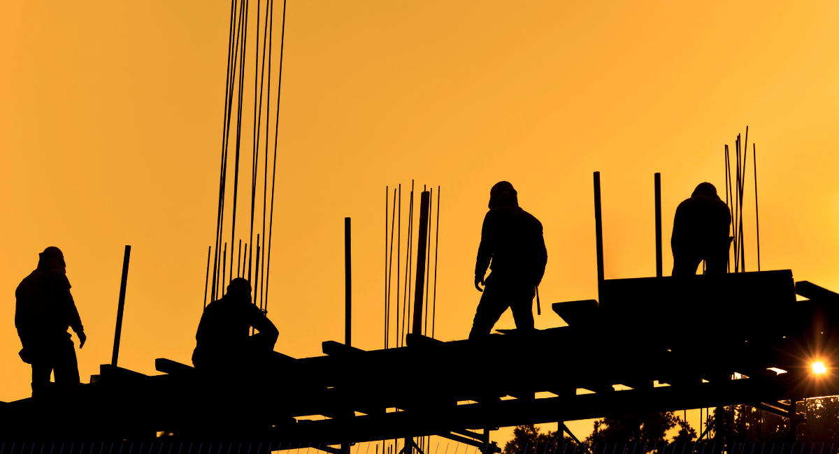 Silhouettes of construction workers standing on building studs against orange sky