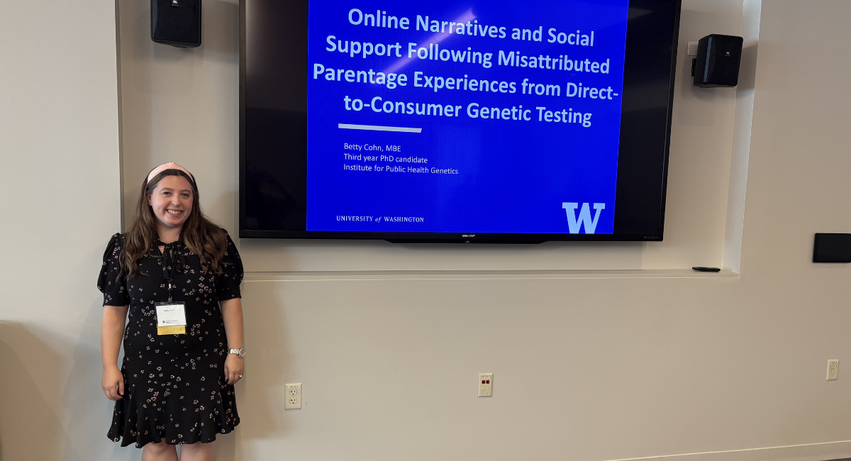 Betty stands in front of digital sign reading "Online Narratives and Social Support Following Misattributed Parentage Experiences from Direct-to-Consumer Genetic Testing