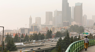 Smoky haze covers Seattle downtown skyscrapers next to freeway and person walking