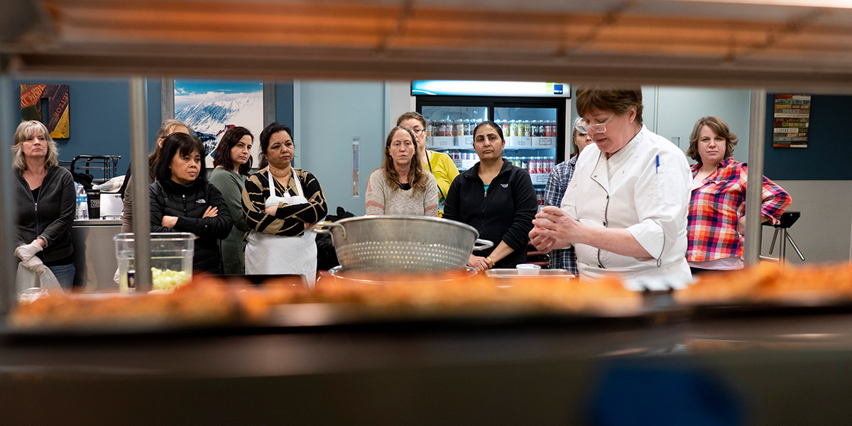 Chef consultant Cathy Powers shows food service staff how to toss fruit salad with cilantro and lime.