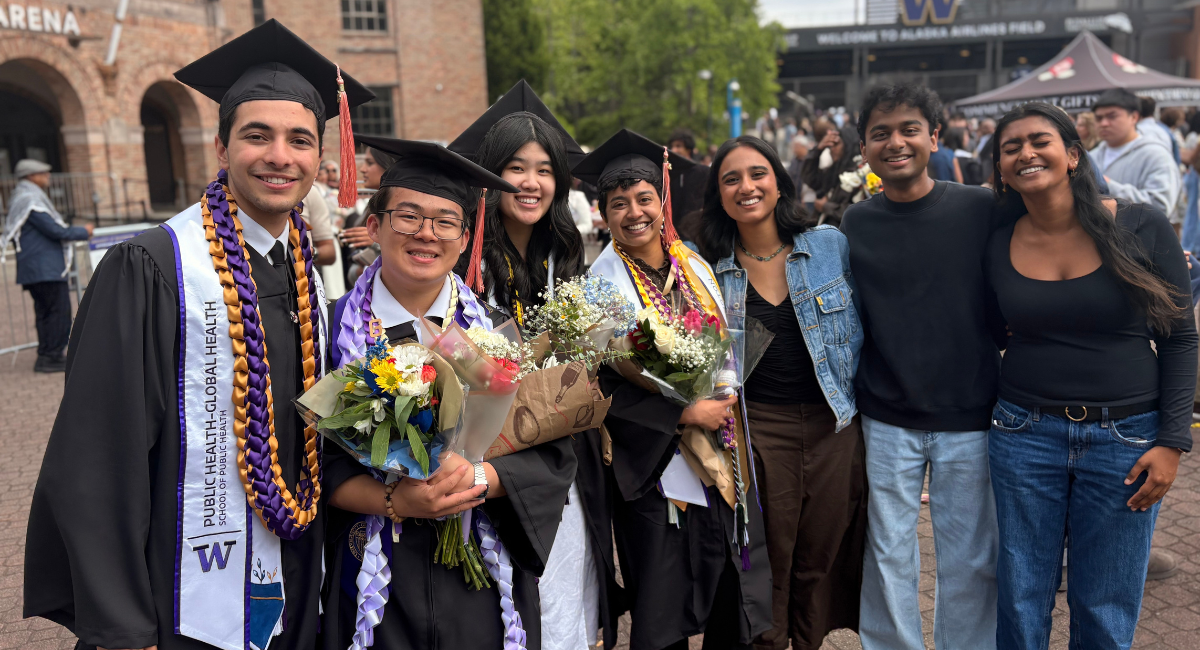 7 people smile together, some wearing graduation hats and holding flowers