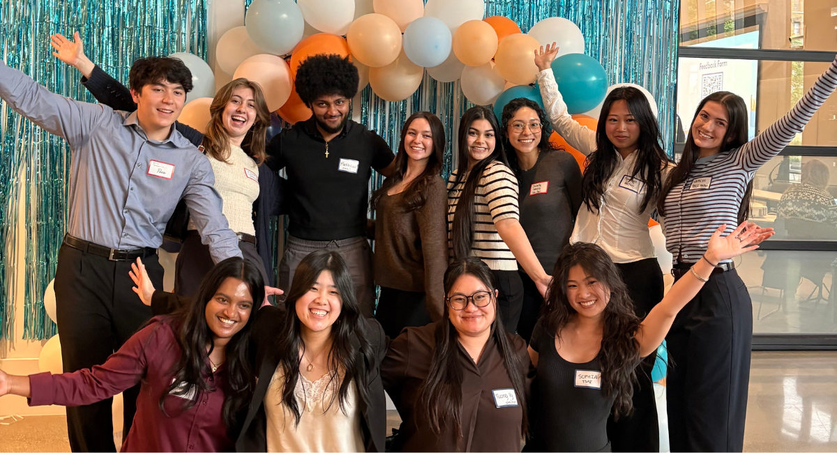 12 students smile in front of balloons and streamers