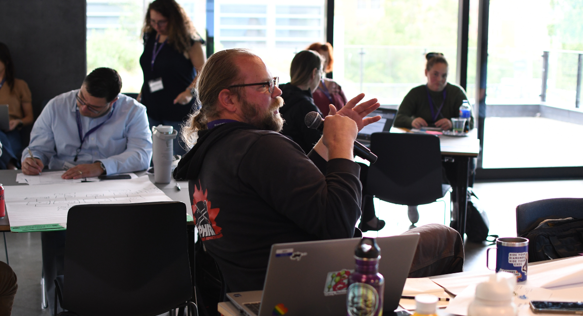 ocean mason speaks into a microphone as people in room look on