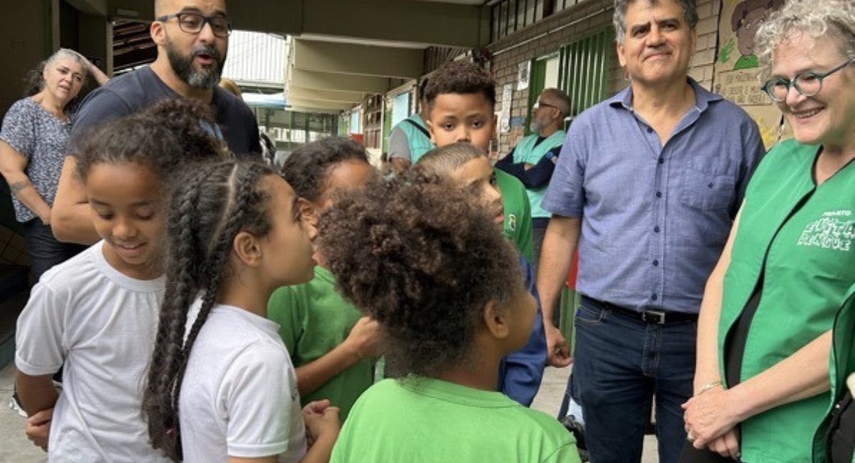 Jeanne smiles at a group of five school children as three adults stand in the background.