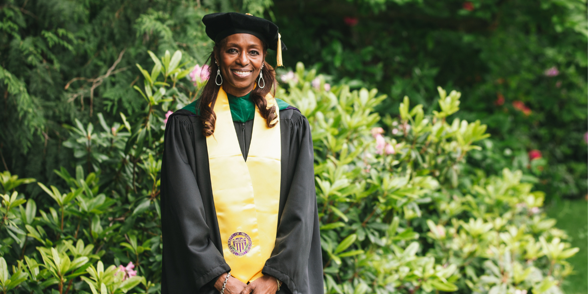 Tapley stands in front of rhododendron in graduation hat and cloak 