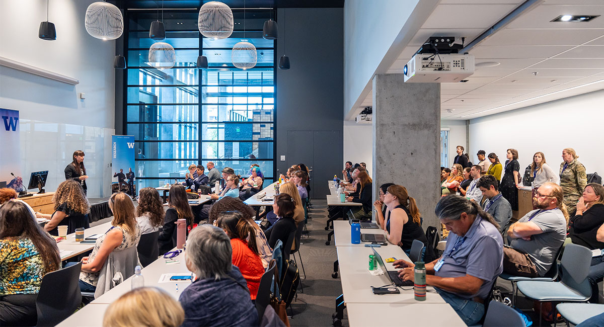 People sit at tables in a room looking at a speaker