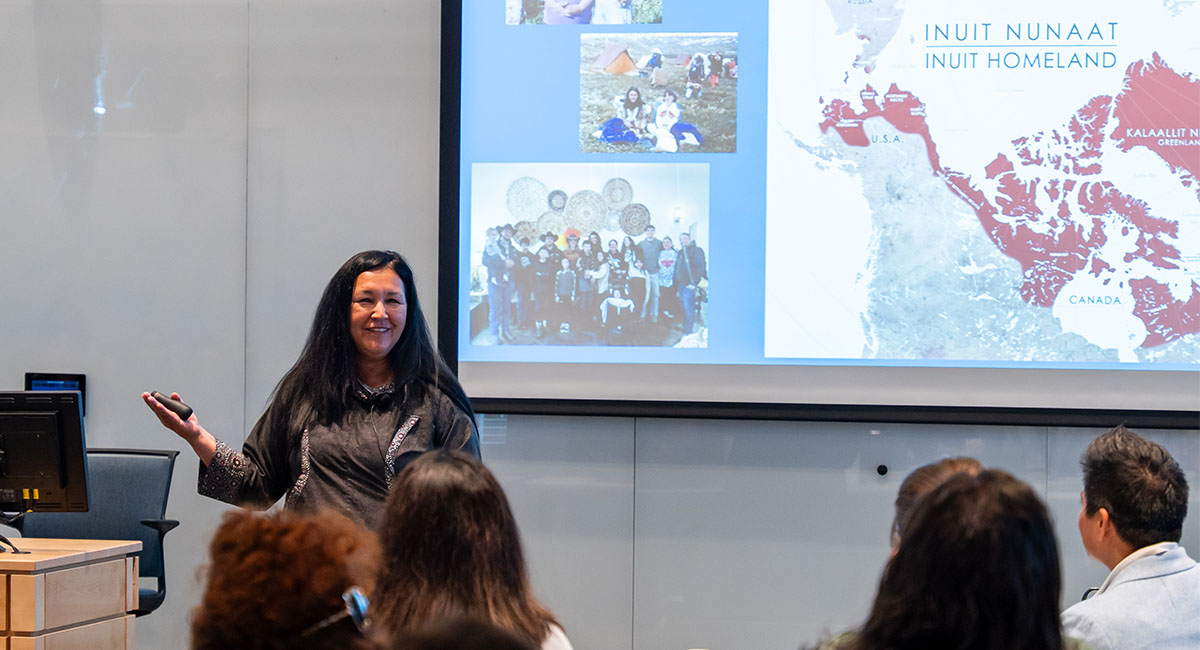 A person stands in front of projected image of Inuit Homelands while people look on