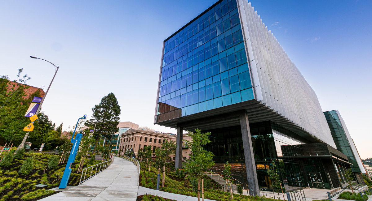 A university campus with glass buildings, a sloped walkway and a staircase leading up to campus.