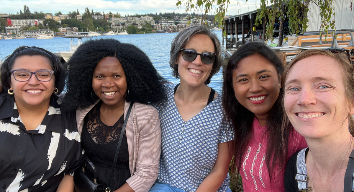 Five people smile and sit in front of lake
