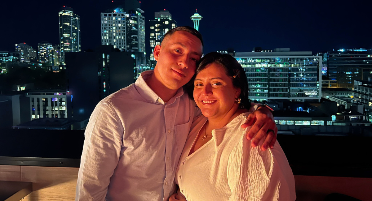 Two people stand together in front of night Seattle skyline