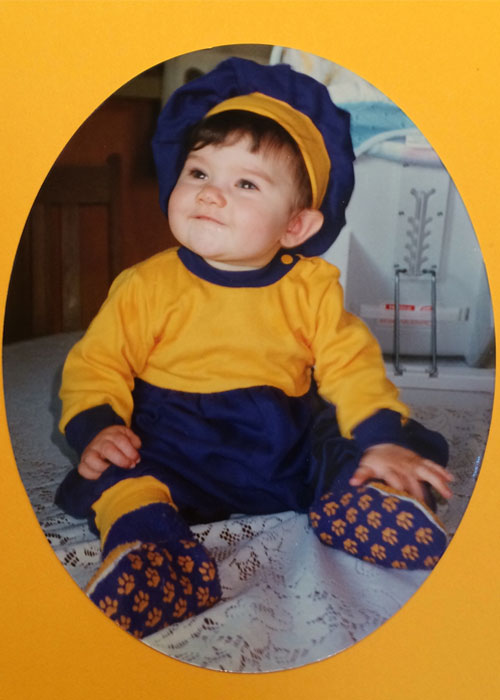 Emma Spickard as a baby, wearing purple and gold.