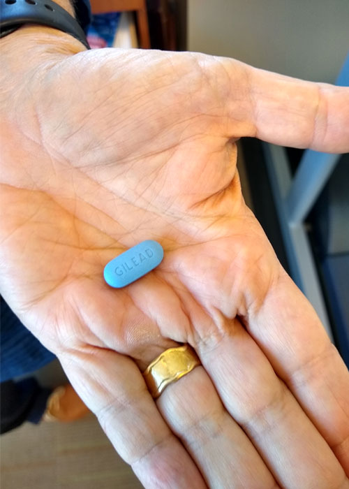 Hand holds a blue Gilead pill, Truvada, used for pre-exposure prophylaxis treatment