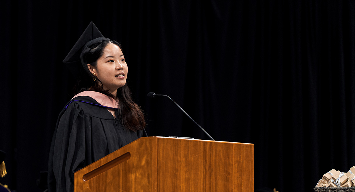 Yifan stands at podium in graduation gown and hat