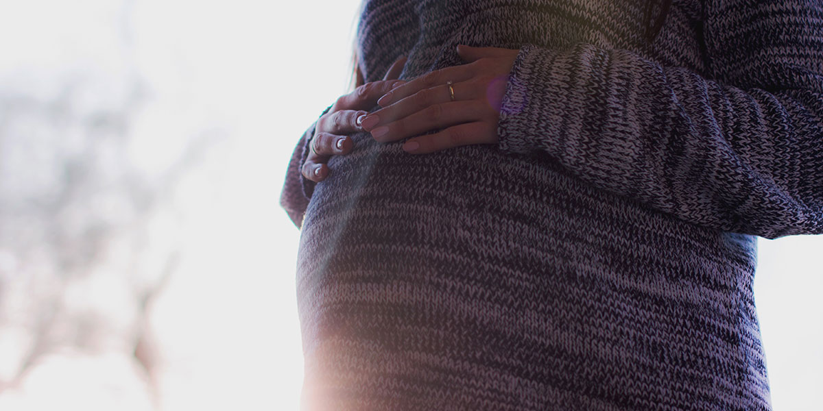 Pregnant woman in sweater resting hands on belly, backlit by the sun - Pexel Images 