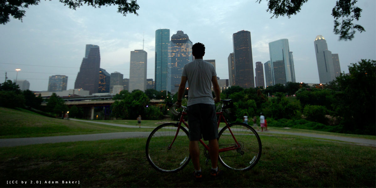 Biker on a bayou trail looks at the Houston skyline [(CC by 2.0) Adam Baker] 